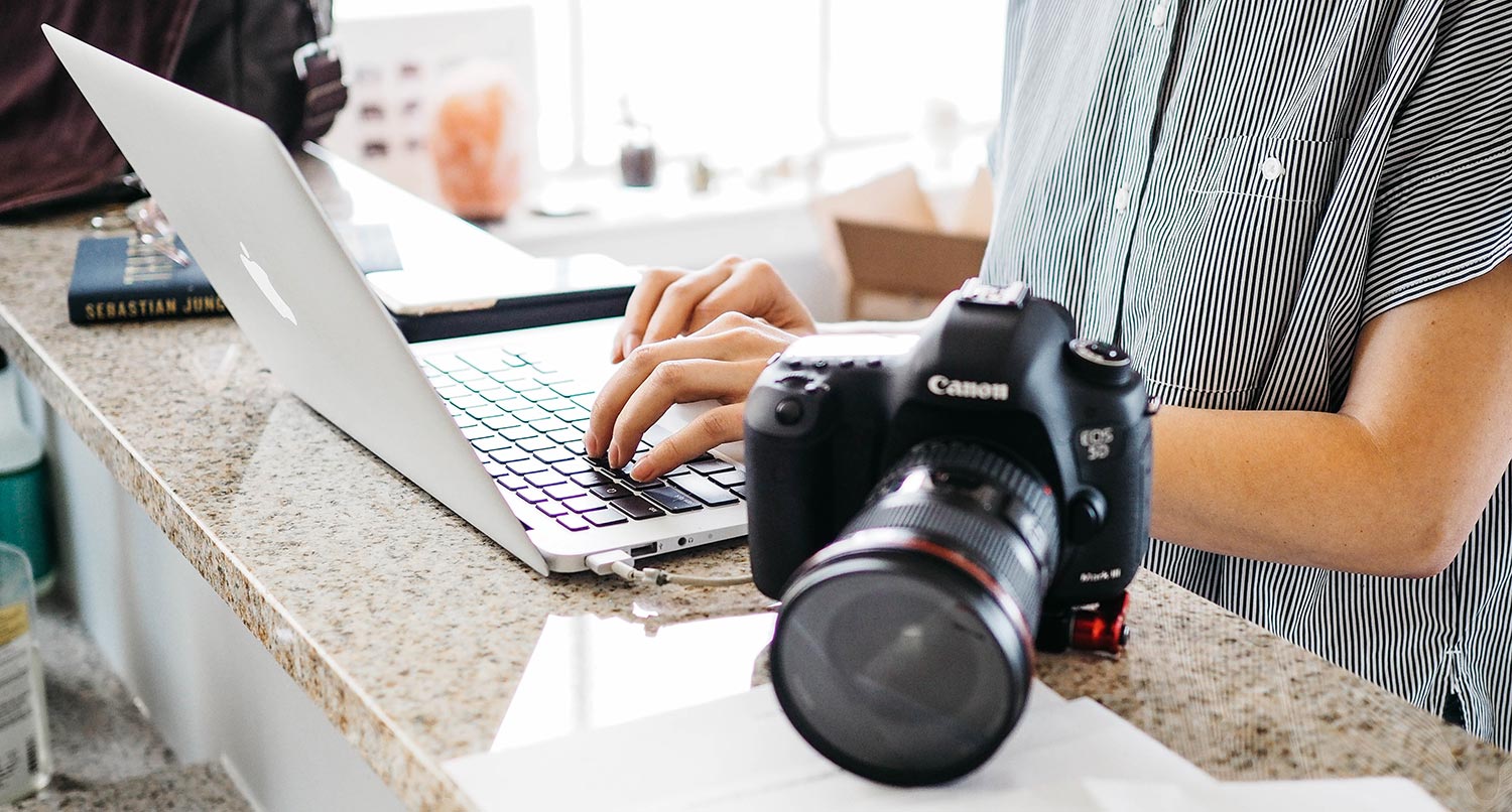 person typing on a laptop with a DSLR black camera next to the laptop