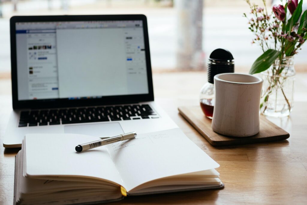 an open notebook sitting on a desk in front of a laptop and next to a cup of coffee